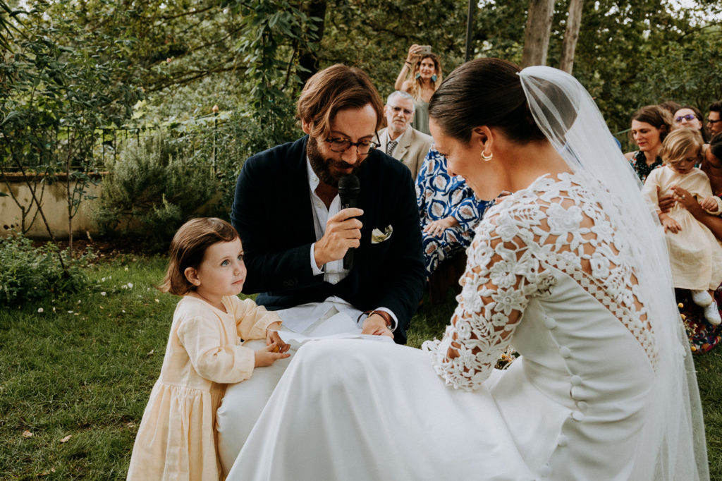 the groom reads his vows while his daughter is holding on to him and looking at the bride